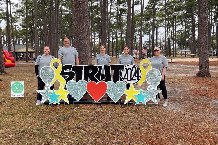 a group of Bryant RE staff members stand in front of a sign that reads "Strut 2024"